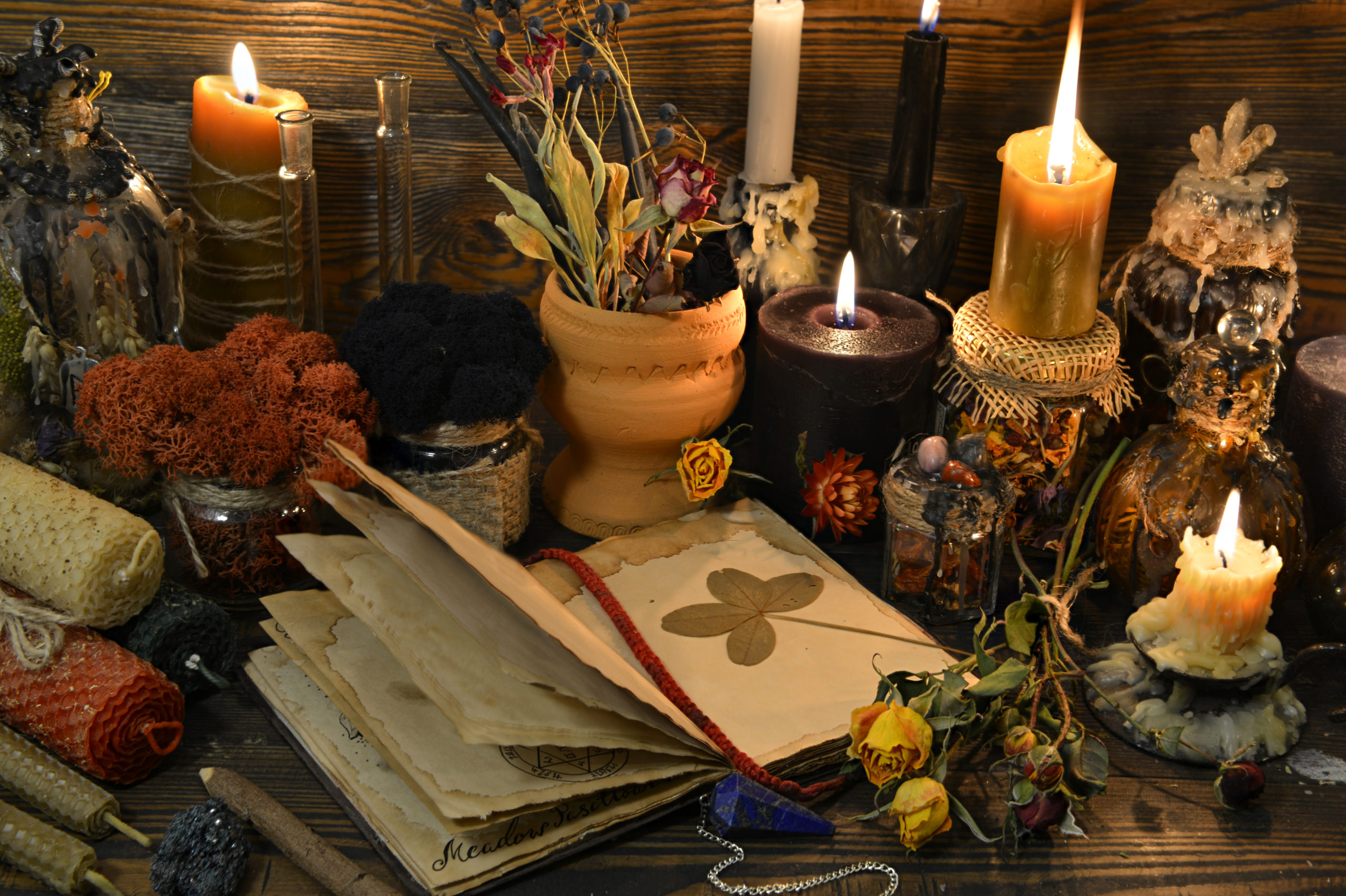 Still life with open book, four-leaf clover, candles and dry flowers on witch table. Esoteric, wicca and occult background, fortune telling and divination ritual, mystic concept