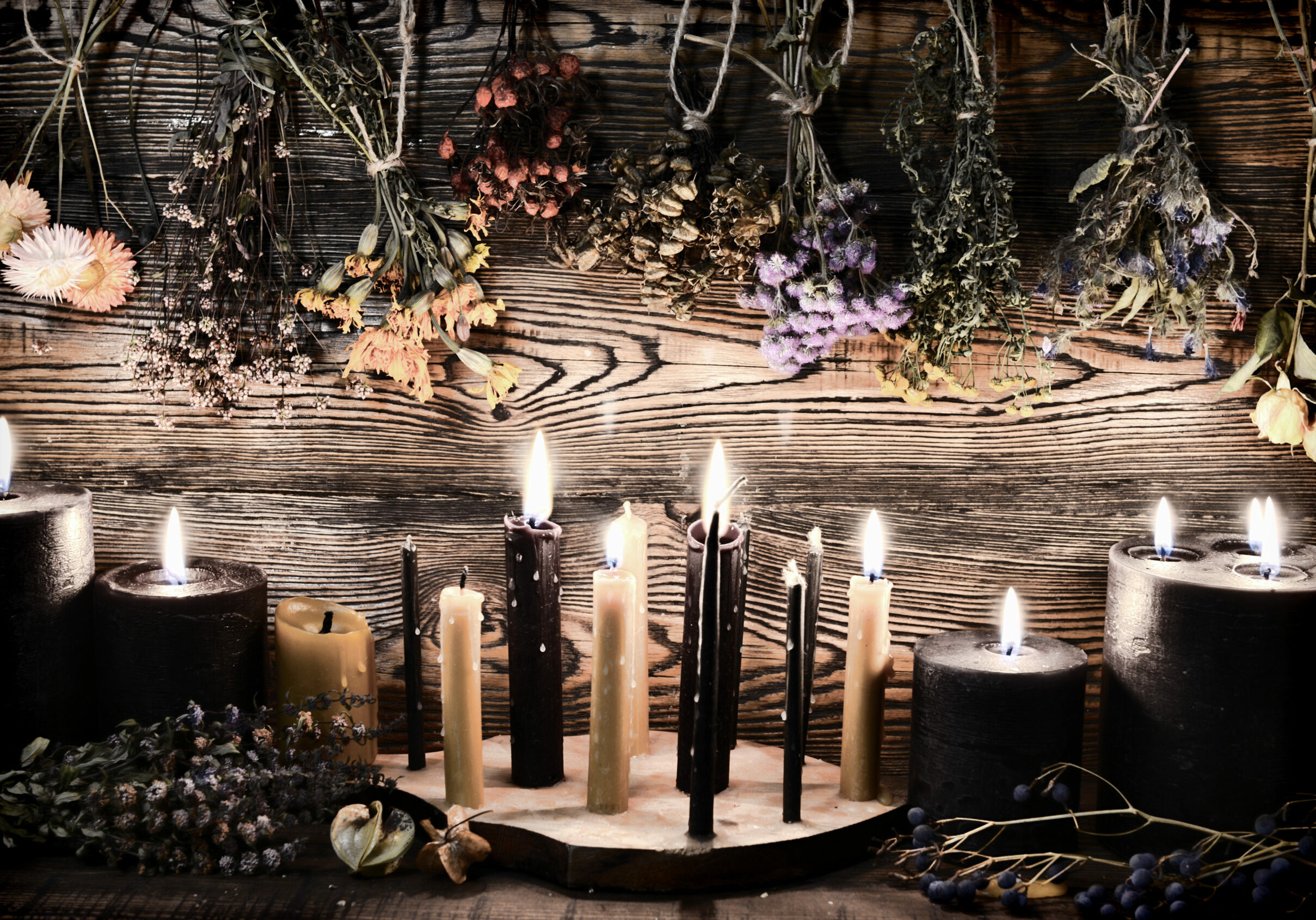 Black candles, herbs and flowers against wooden wall on witch table. Esoteric, wicca and occult background, fortune telling and divination ritual, mystic concept