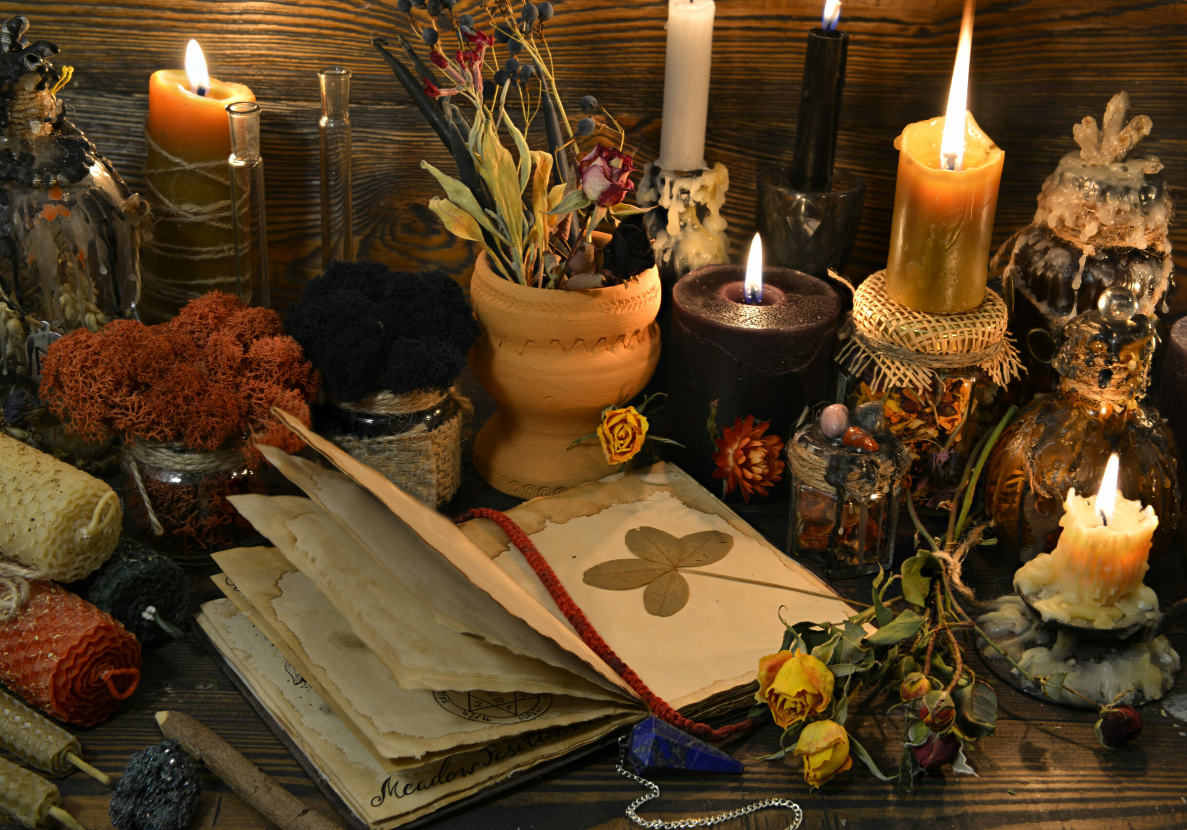 Still life with open book, four-leaf clover, candles and dry flowers on witch table. Esoteric, wicca and occult background, fortune telling and divination ritual, mystic concept